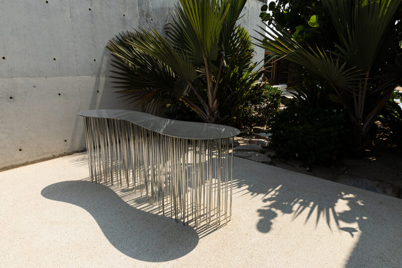 Photo by Gerardo Maldonado of Rainfall console table set outside on concrete floor against backdrop of tropical palm plants.