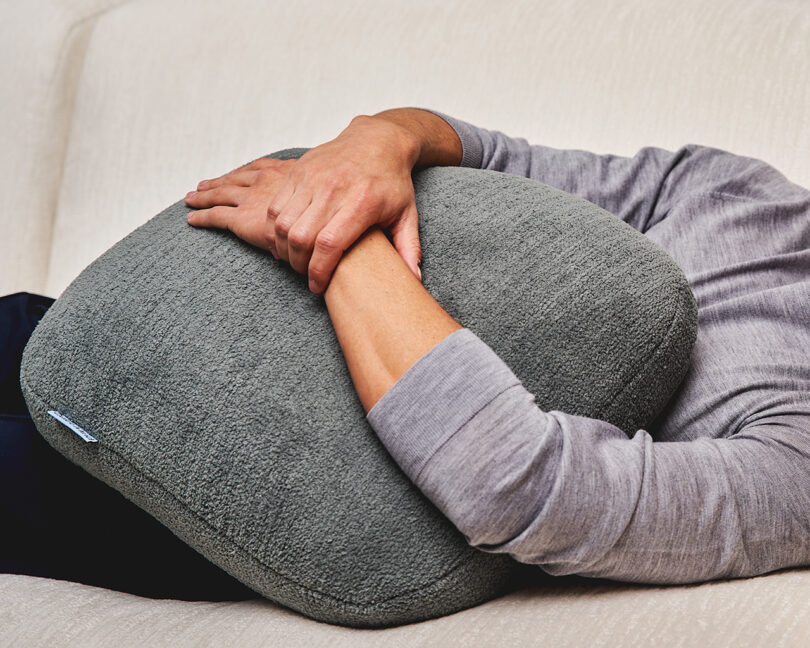 light-skinned arms holding on to a grey square pillow