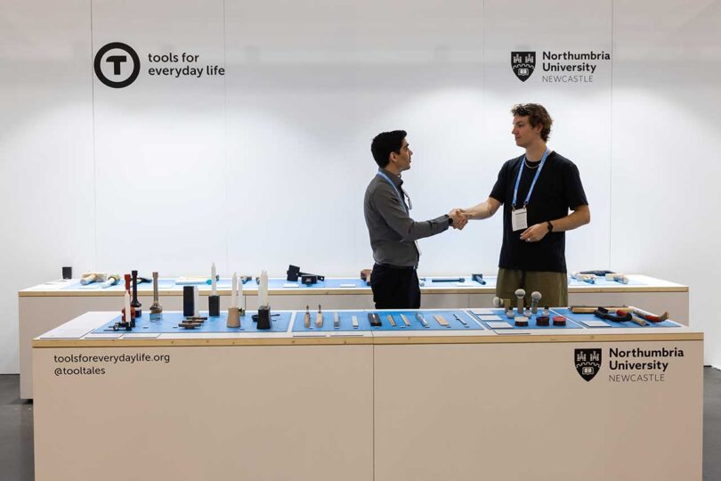 booth at trade show featuring two tables of designs with two men shaking hands