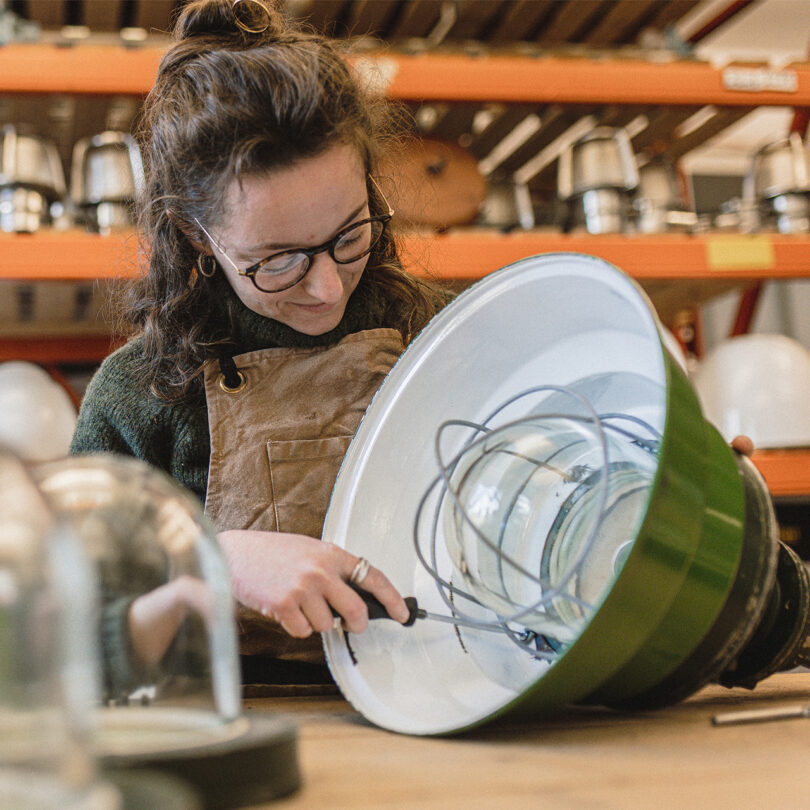 A white women in her 30s holds a screwdriver to the inside of a pendant light