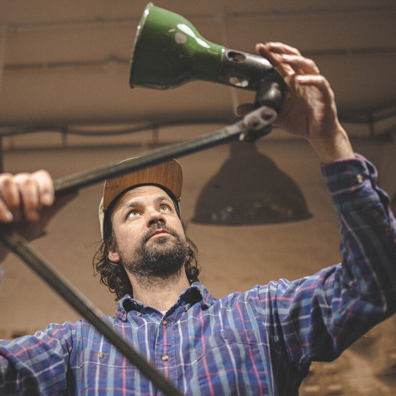 A white man in a shirt and cap adjusts a desk lamp