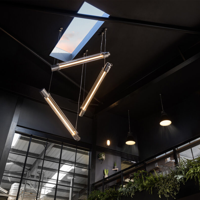 Three strip lights hang from a black-painted high ceiling 